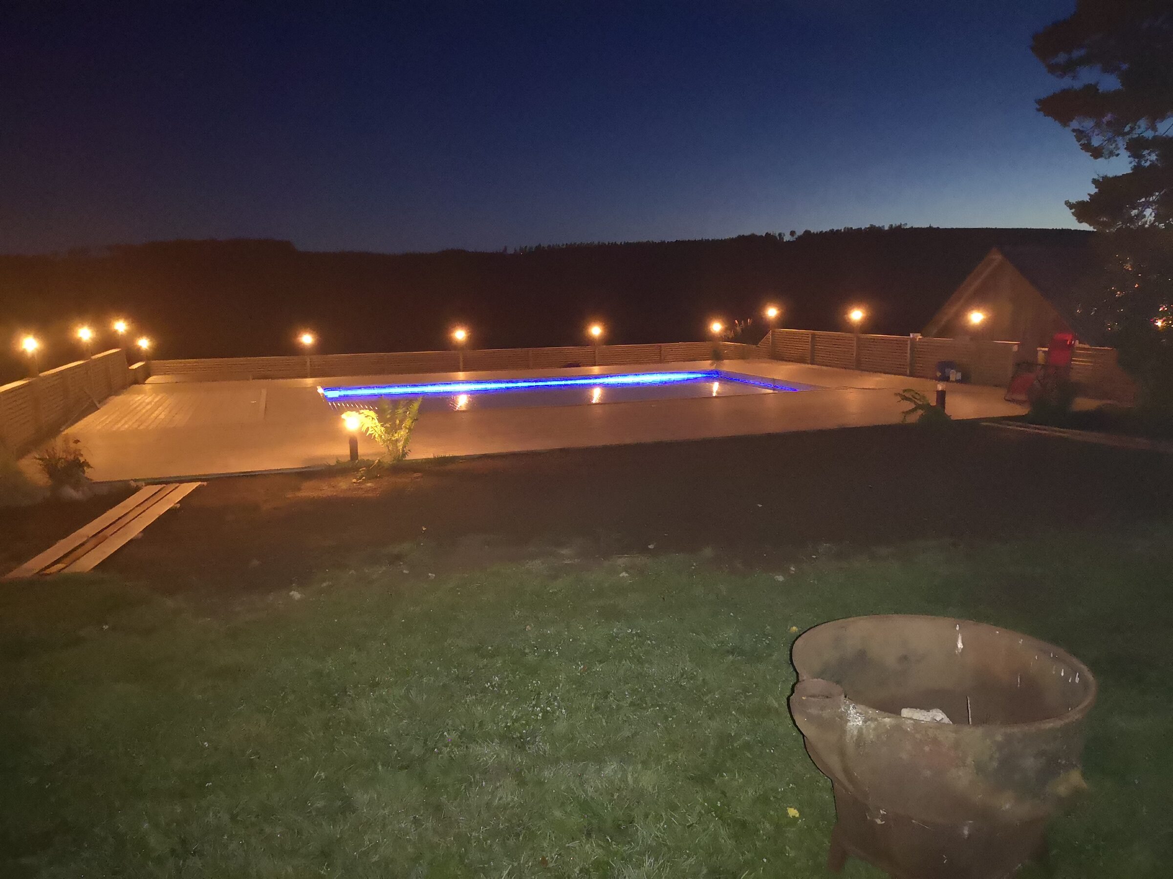 Kvällsbelyst pool och spabad framför upplyst villa i skymningen — poolmiljö monterad av The Pool Guy