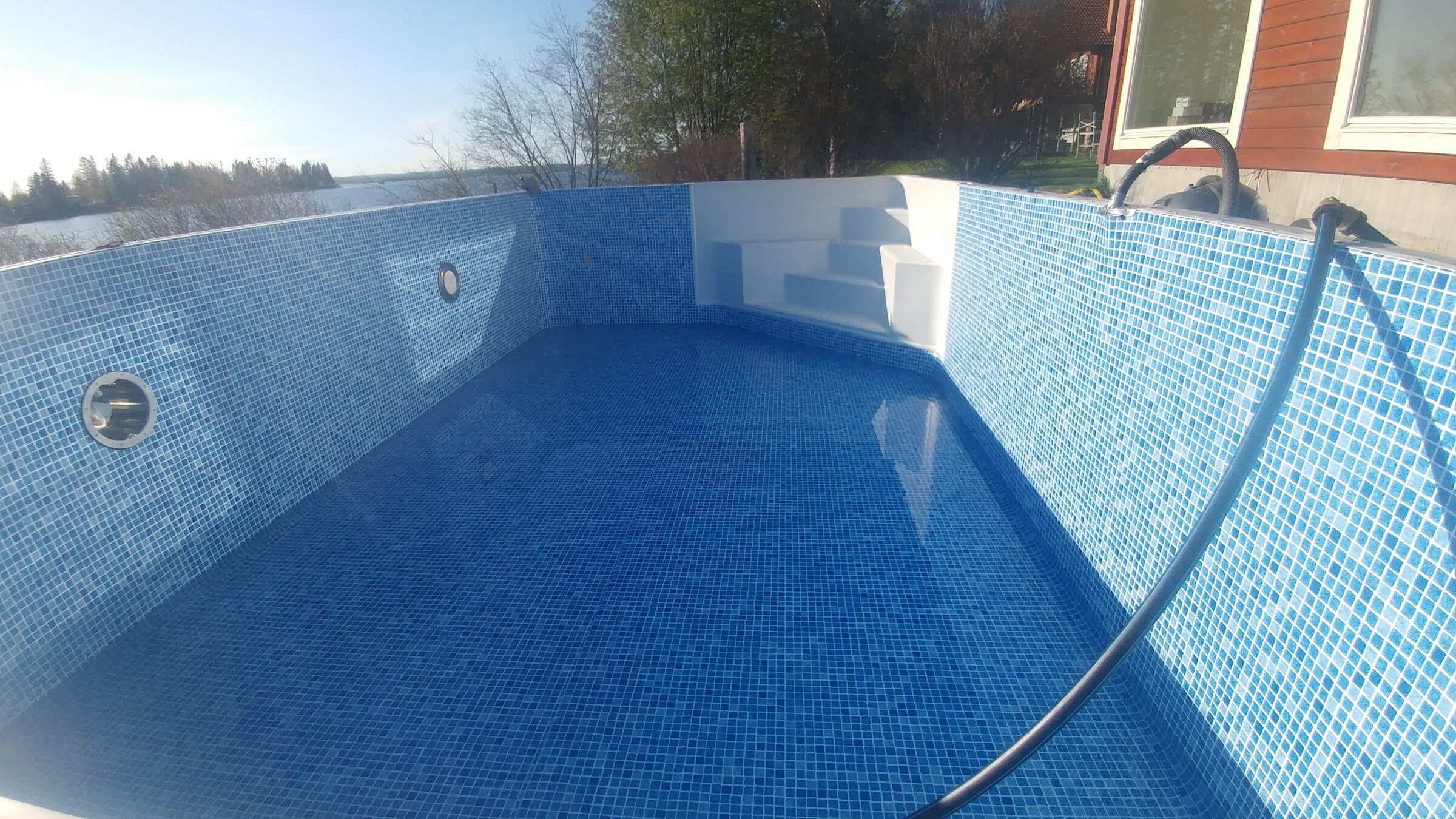 Mosaikklädd pool med trädäck ända ned mot vattnet
